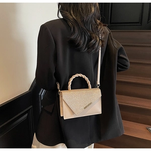 Sac à paillettes champagne avec poignée tressée porté sur un mannequin en tailleur noir