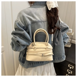 Detailed view of cream shell-shaped handbag with decorative straps on model back