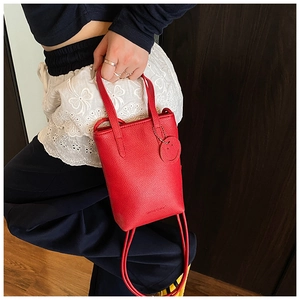 Detail of red pebbled leather handbag featuring a round smiley face charm and thin strap