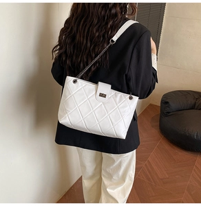 Detail of white quilted tote bag with silver metal turn-lock and chain shoulder strap