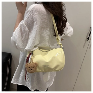 Detail of light yellow leather crossbody bag with teddy bear charm and silk scarf accent