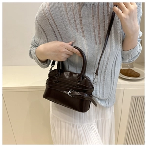 Detail of dark brown shell bag with buckle strap on a model in a minimal French setting