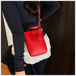 Detail of red litchi texture leather mini handbag with round smiley pendant accessory