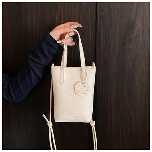 Close-up of cream lychee texture leather mini tote with smiley pendant and thin strap