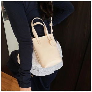 Macro detail of cream lychee-textured leather tote bag with smile charm and shoulder strap