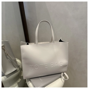 Detail shot of white leather tote bag with embossed letters on a minimalist display