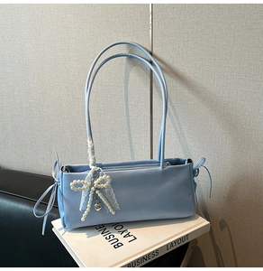 Close-up of light blue shoulder bag with lace bow, beads and silver heart pendant detail
