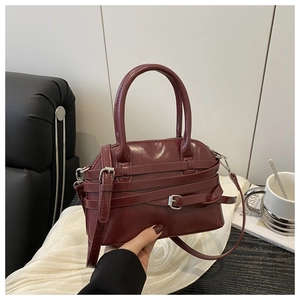 Detail shot of wine red glossy leather tote featuring decorative straps and silver buckles