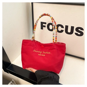 Detail of red canvas tote bag with embroidered letters and colorful striped woven handle