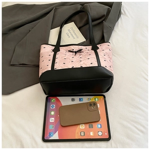 Pink tote bag with black bows and leather trim shown next to a tablet for size scale