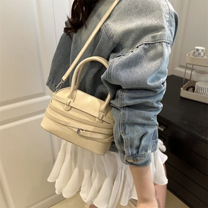 Chic cream shell-shaped crossbody bag with decorative belts and silver buckles