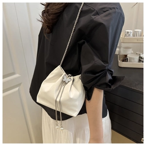 Détail du sac seau blanc gaufré avec chaîne argentée, breloque papillon et perles