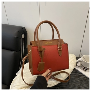 Detail of red lychee grain leather handbag with brown flap and gold logo text