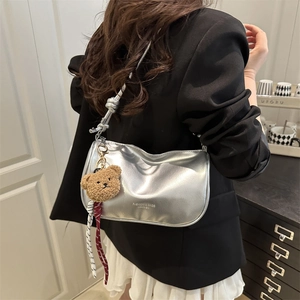 Silver metallic crescent crossbody bag with knotted strap and plush bear charm worn by model