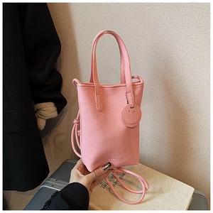 Detail of pink lychee leather tote with thin round strap and smiley face pendant charm