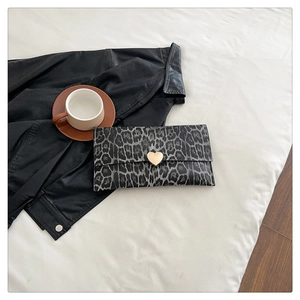 Détail de la pochette léopard avec un fermoir en forme de cœur doré sur tissu blanc