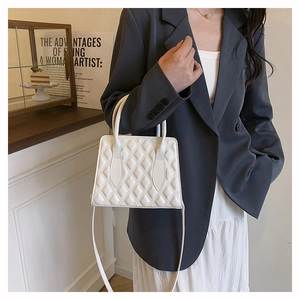Detail showing white quilted diamond pattern on minimalist leather handbag with top handles