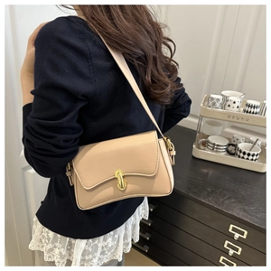 Side view of beige shoulder bag with gold twist lock worn by a model in soft home lighting