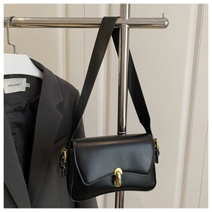 Detailed close-up of a minimalist black leather shoulder bag with a gold oval metal buckle