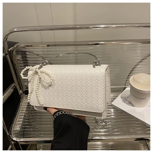 Detail of white woven texture bag with pearl bow decoration and silver metal handle