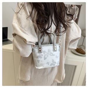 Detail of a beige butterfly print handbag with grey strap and bronze hardware details