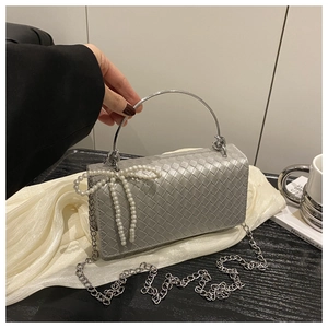 Detail of silver woven handbag featuring a pearl bow ornament and metal ring handle