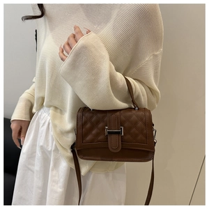 Gros plan d'un sac à bandoulière matelassé marron avec boucle argentée porté par un modèle