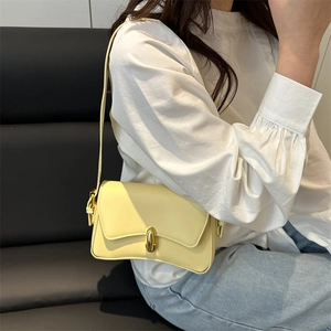 Minimalist light yellow shoulder bag with gold metal clasp on a leather sofa background