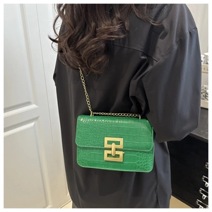 Detail of green faux crocodile leather bag with gold chain and geometric twist lock