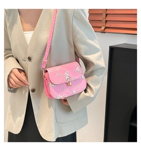 Close-up of a pink crossbody bag featuring delicate white floral embroidery and gold buckle