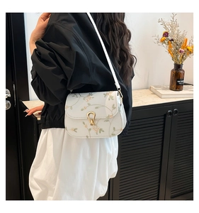 Detail of floral lace embroidery and golden drop lock on a white elegant crossbody bag