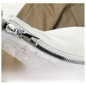 Détail de la broderie à paillettes blanches avec une fermeture éclair en métal argenté