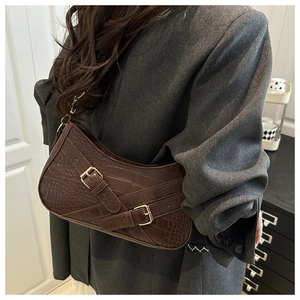 Detail of dark brown faux crocodile baguette bag with golden buckle straps on shoulder