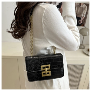 Detail of black crocodile texture bag with gold geometric clasp and metal chain strap