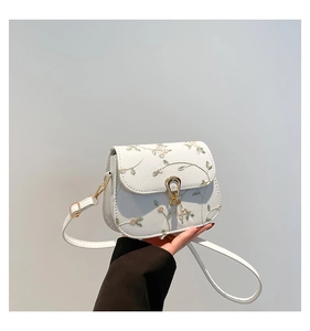 Close-up of white crossbody bag with floral embroidery and golden teardrop lock