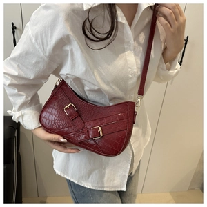 Detail of burgundy crocodile-textured bag with gold buckles worn as a shoulder bag