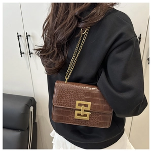 Detail of dark brown croc-embossed crossbody bag with square gold lock on shoulder