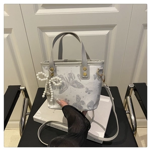 Detail of white bucket bag featuring silver butterfly jacquard and pearl bow charm accessory