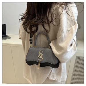 Close-up of gray textured handbag with golden S logo, fringe detail and black trim