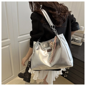 Detail of silver metallic tote bag with chain strap, plush charm, and decorative scarf