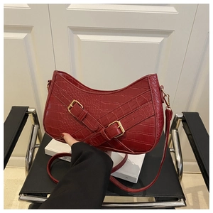 Detailed macro of burgundy faux crocodile texture shoulder bag with gold buckles