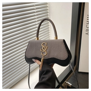 Close-up of stylish handbag featuring grey woven flap and golden SSS metal logo with tassel