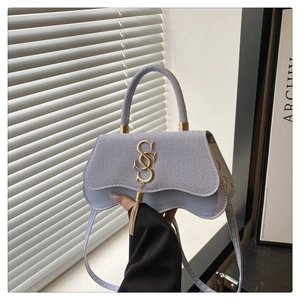 Detail of light blue handbag with woven texture flap, golden SSS logo and metal tassel