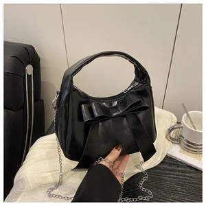 Détail du sac en cuir brillant noir avec nœud décoratif et bandoulière en chaîne