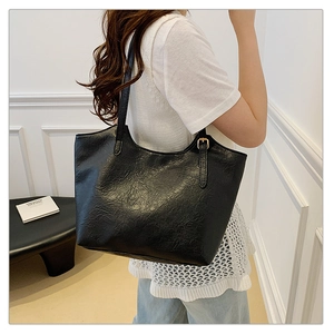 Detail of black faux leather tote with oily texture and adjustable strap on a shoulder