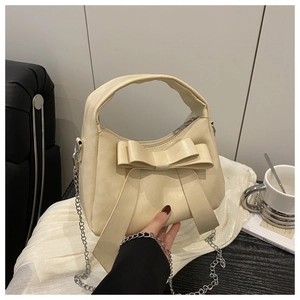 Sac bandoulière beige avec nœud et chaîne argentée élégante dans un cadre décontracté