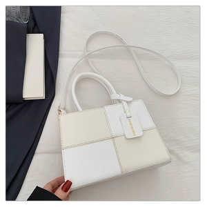 Detail of checkered faux leather crossbody bag with top handle and brand tag on white fabric