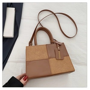 Detail view of brown patchwork handbag with gold-stamped tag on minimalist white fabric