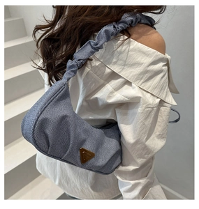 Macro view of light blue denim hobo bag with pleated strap and golden triangular logo