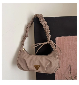 Detail of a pleated strap on a beige crescent bag with triangular metallic hardware